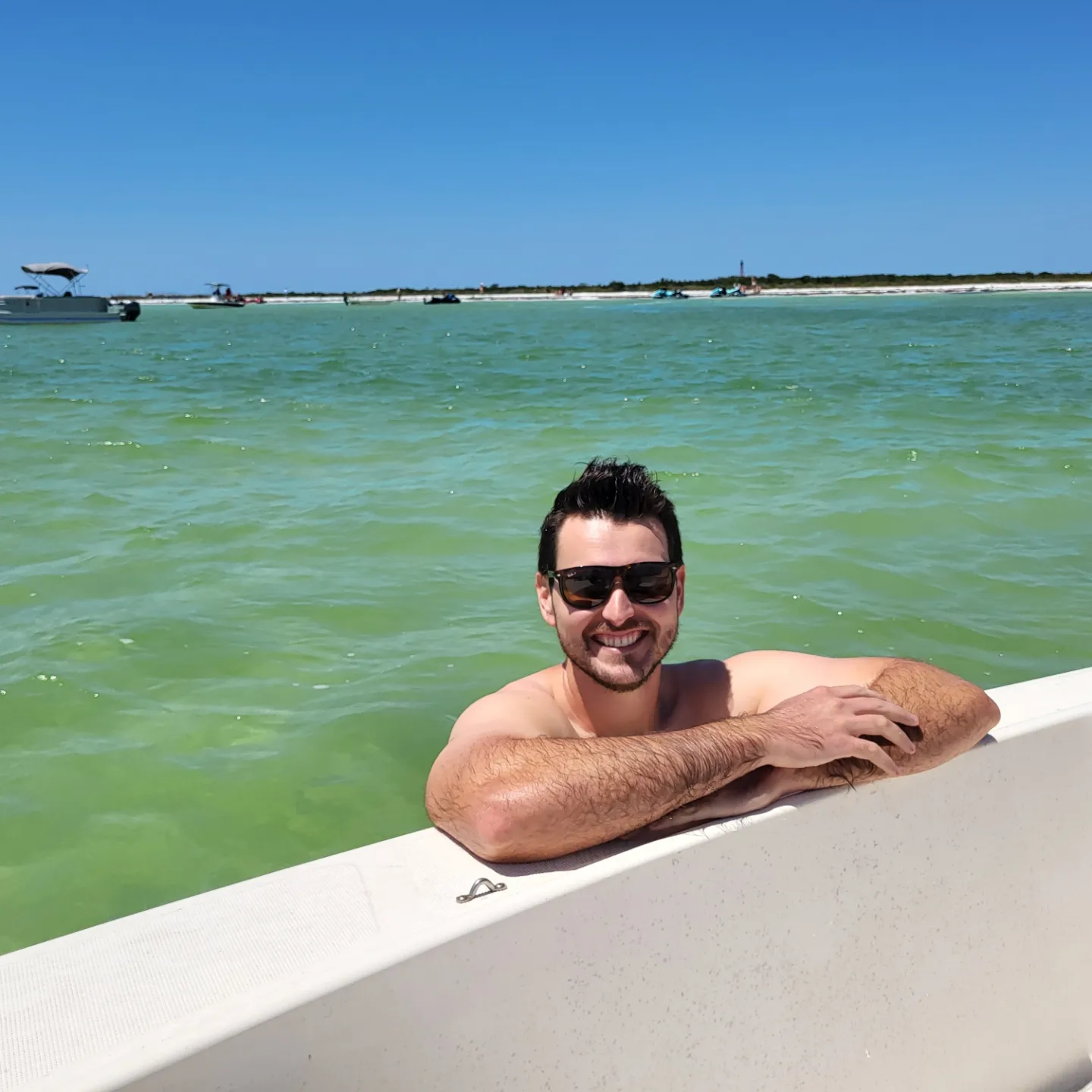 Aric in the water next to a boat in the Cedar Keys National Wildlife Refuge, lighthouse on Seahorse Key in the background